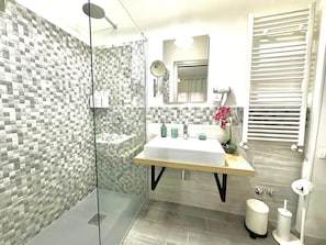 Een moderne badkamer met een douchecabine van glas, een witte wastafel en een spiegel erboven.