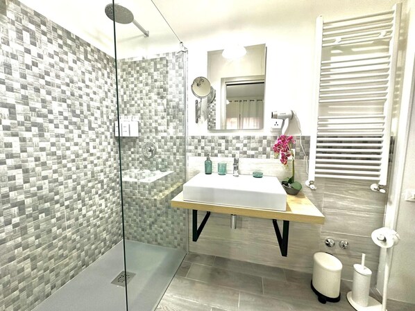 A modern bathroom with a glass shower enclosure, a white sink, and a mirror above it.