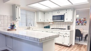 A modern kitchen with white cabinetry, a central island, a microwave, and a dining area with a table and chairs.