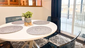 A round dining table with a white tablecloth, four grey placemats, and a potted plant in the center.