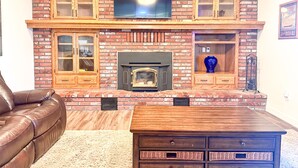 A living room with a brick fireplace, a television mounted above it, and wooden cabinets.