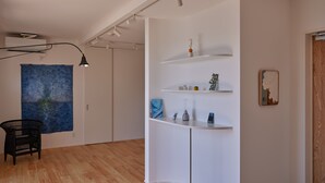 A modern room with a wooden floor, white walls, a black chair, a blue painting, and a white shelving unit with decorative items.