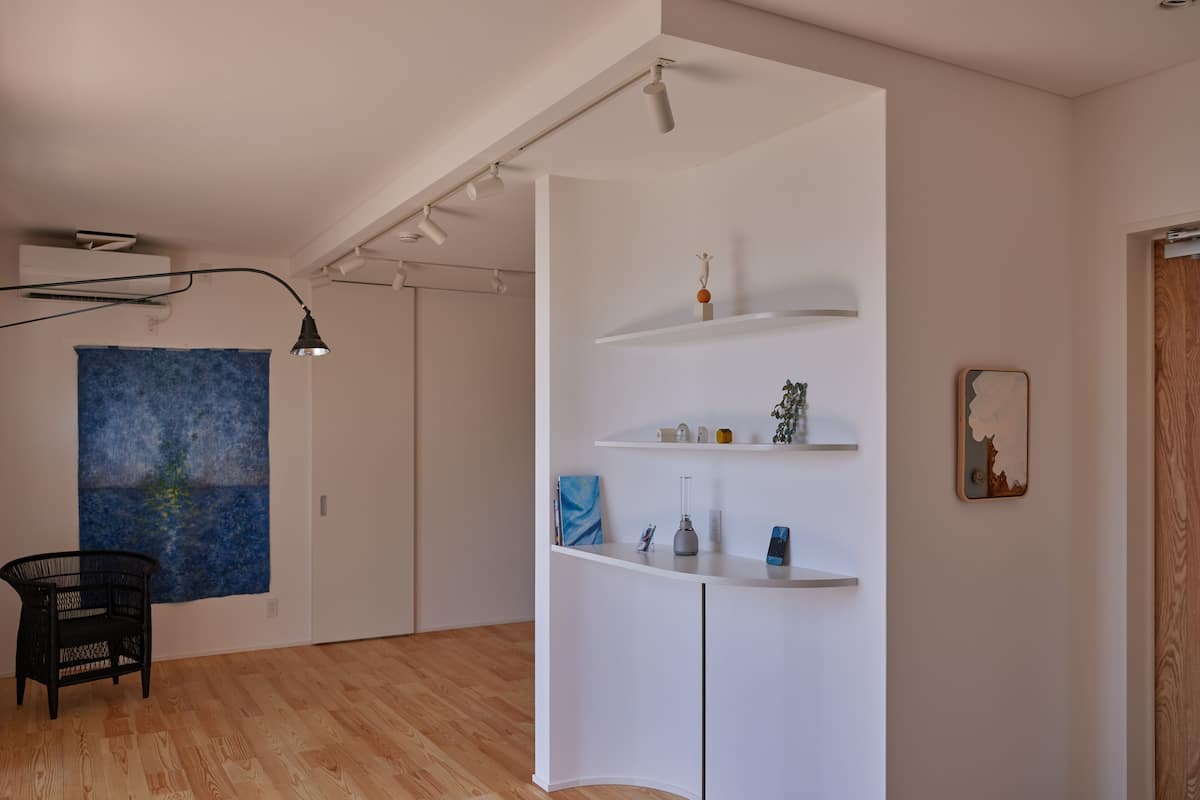 A modern room with a wooden floor, white walls, a black chair, a blue painting, and a white shelving unit with decorative items.