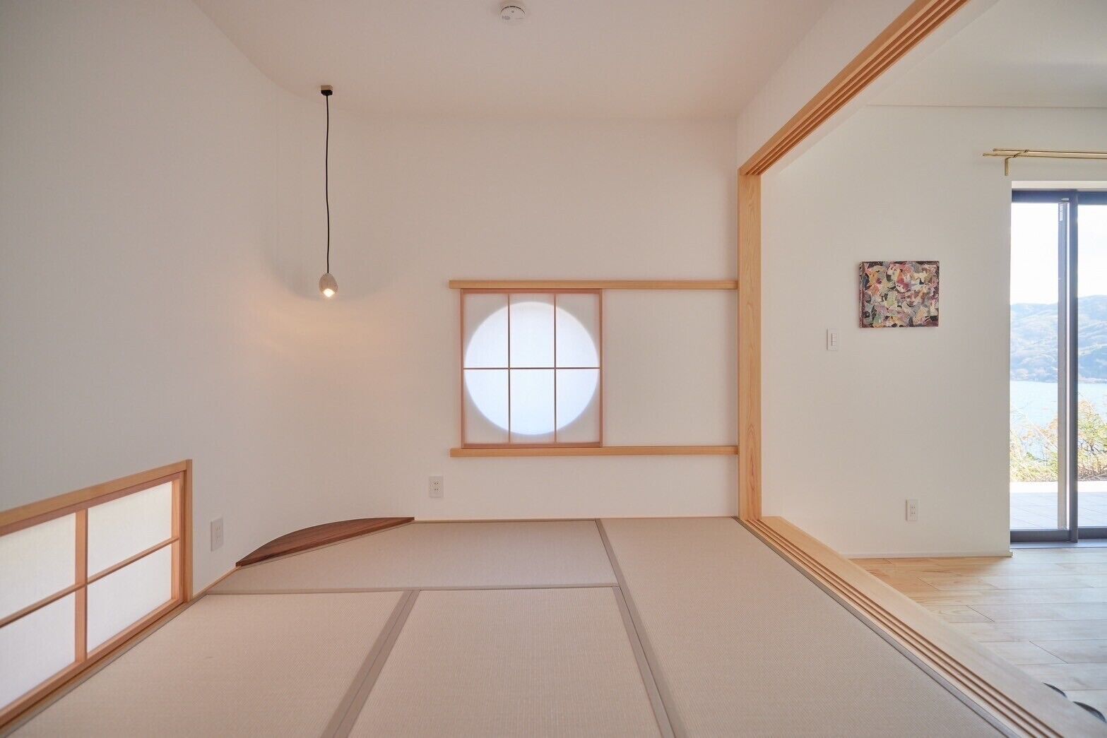 A minimalist room with tatami flooring, a shoji screen window, and a view of a lake.
