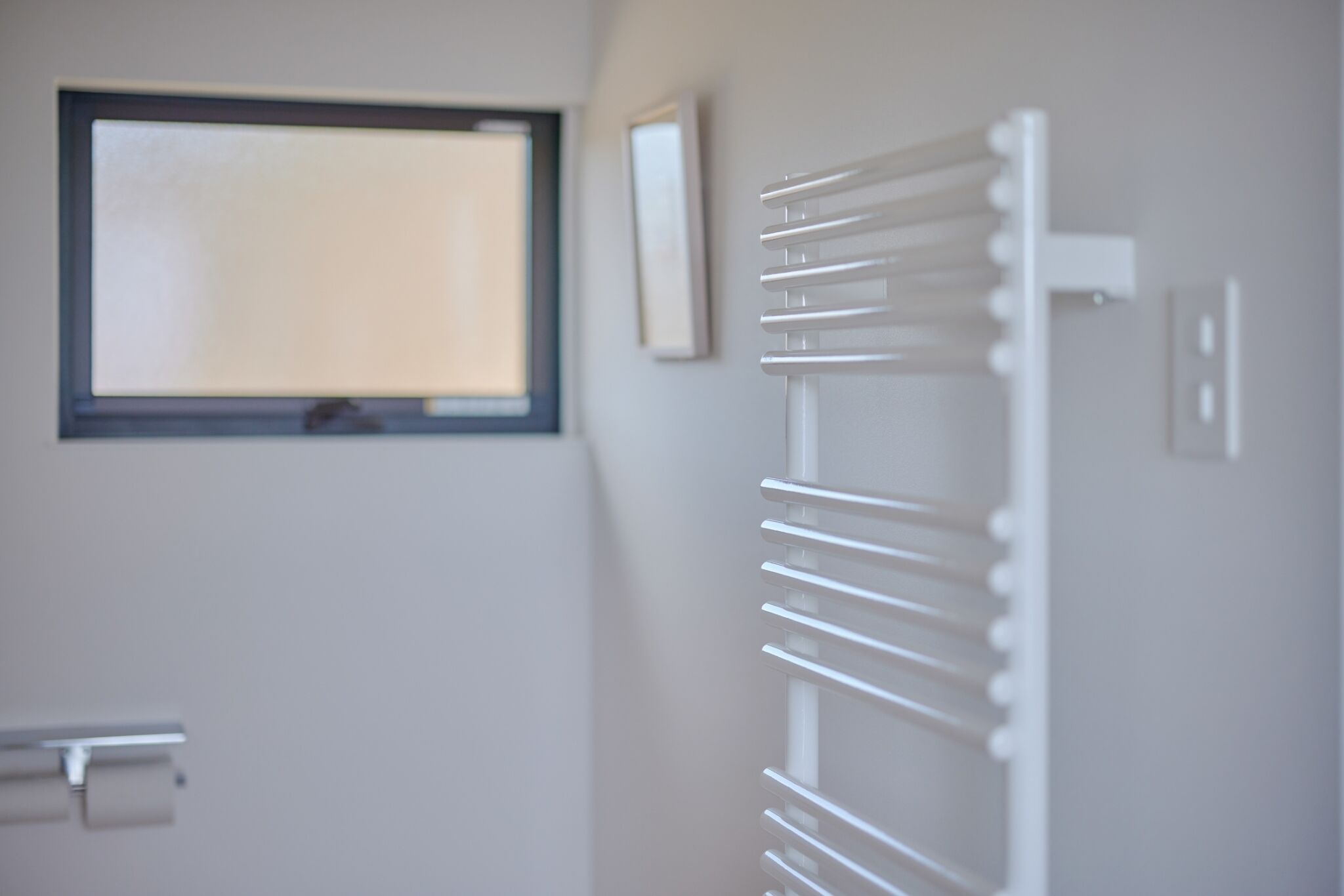 A bathroom with a window, a towel rack, and a toilet paper holder.