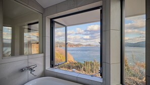 A bathroom with a large window offering a view of a lake and mountains.
