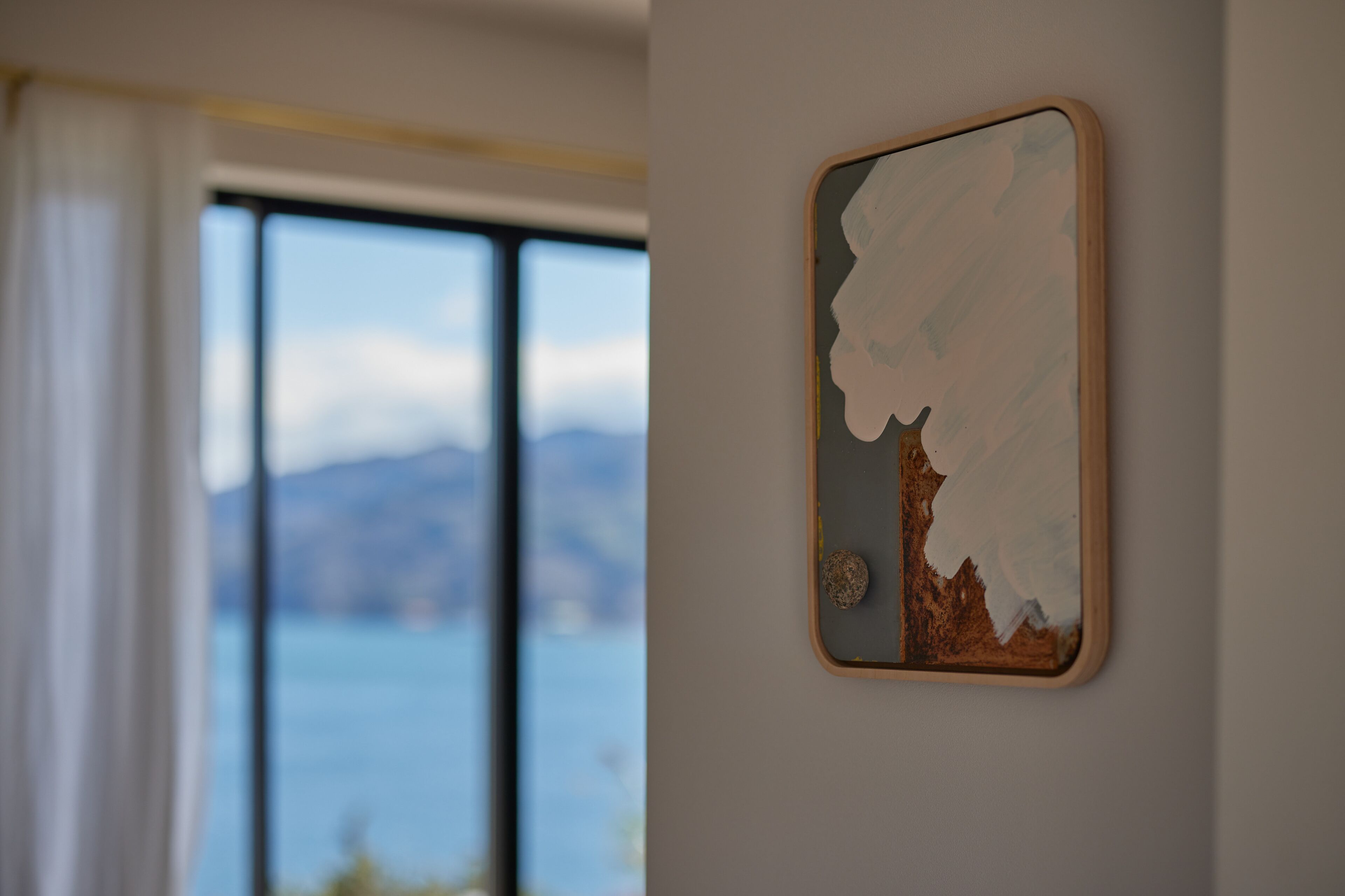 Una obra d'art emmarcada a la paret, amb una vista d'aigua i muntanyes al fons.