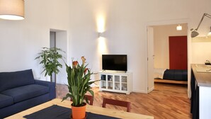 A modern living room with a sofa, a dining table with a potted plant, a TV on a white cabinet, and a red door in the background. - Bright and confortable apartment in the center of the liveliest part of the city (Napoli)