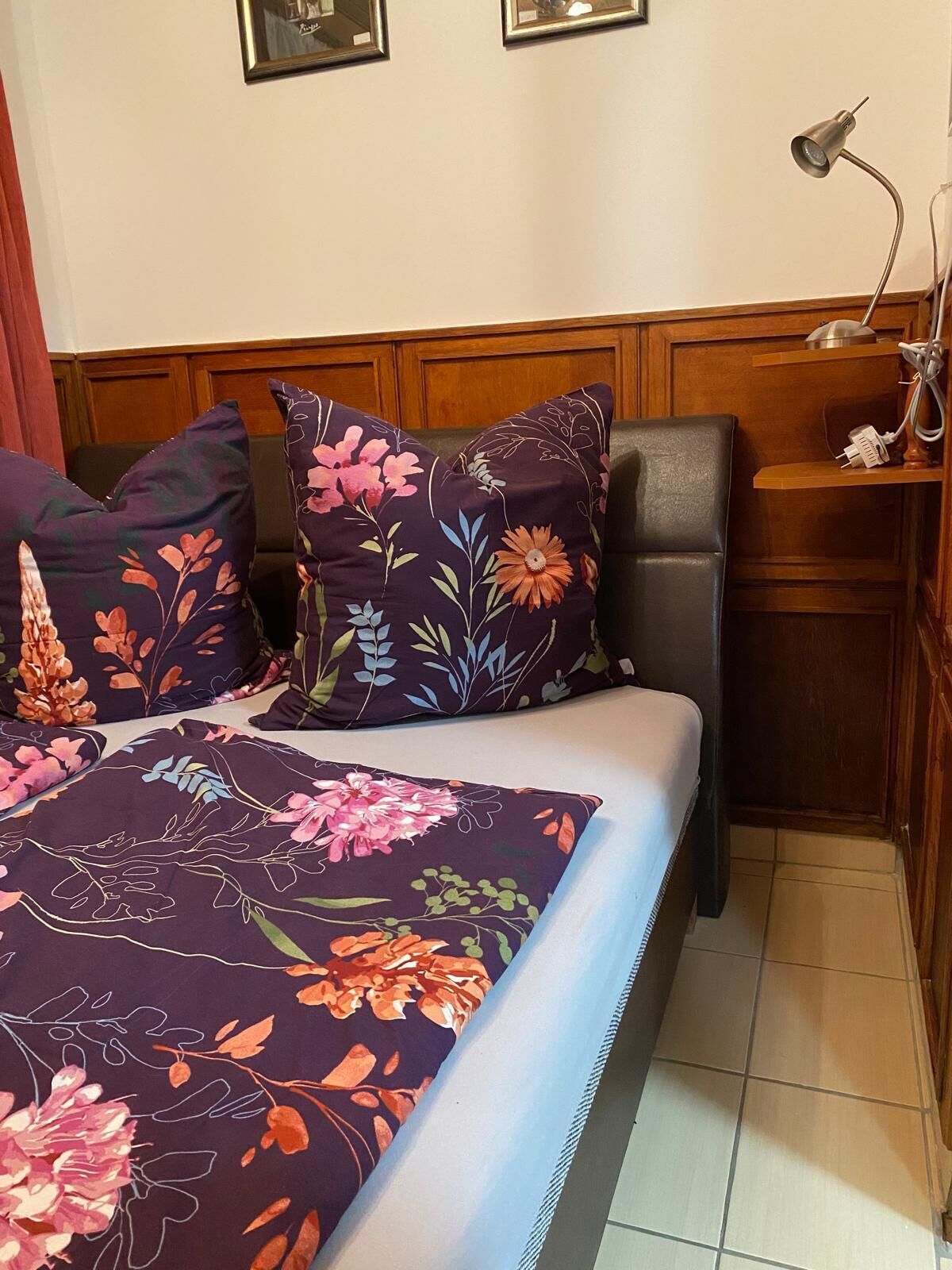 Ein Bett mit floraler Bettwäsche, einer Nachttischlampe und einem Holzkopfende.