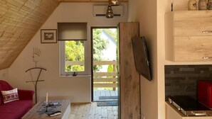 A room with wooden beams, a red sofa, a coffee table, a TV, and a kitchen area with a stove. - Müllers Ferienhaus Harmonie (Dombovar)
