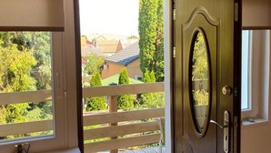 A wooden door with a glass panel, a wooden balcony, and a view of a residential area. - Müllers Ferienhaus Harmonie (Dombovar)