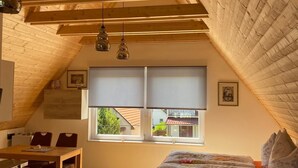 A bedroom with a sloped ceiling, a bed, a window with blinds, a desk, and a chair. - Müllers Ferienhaus Harmonie (Dombovar)