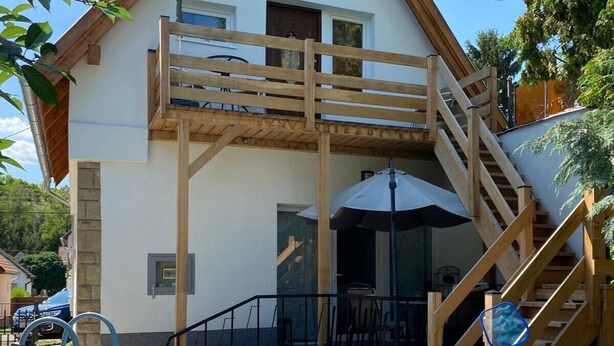 A pool with wooden deck, a covered patio, and a two-story building with a balcony. - Müllers Ferienhaus Harmonie (Dombovar)
