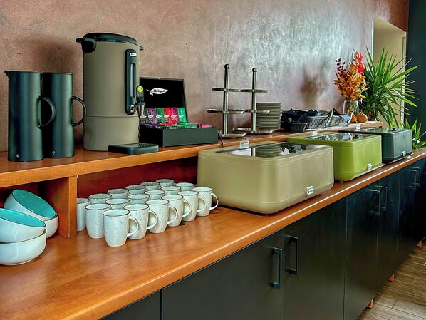 Una barra de desayuno con máquinas de café, dispensadores de té y una variedad de tazas y tazones.