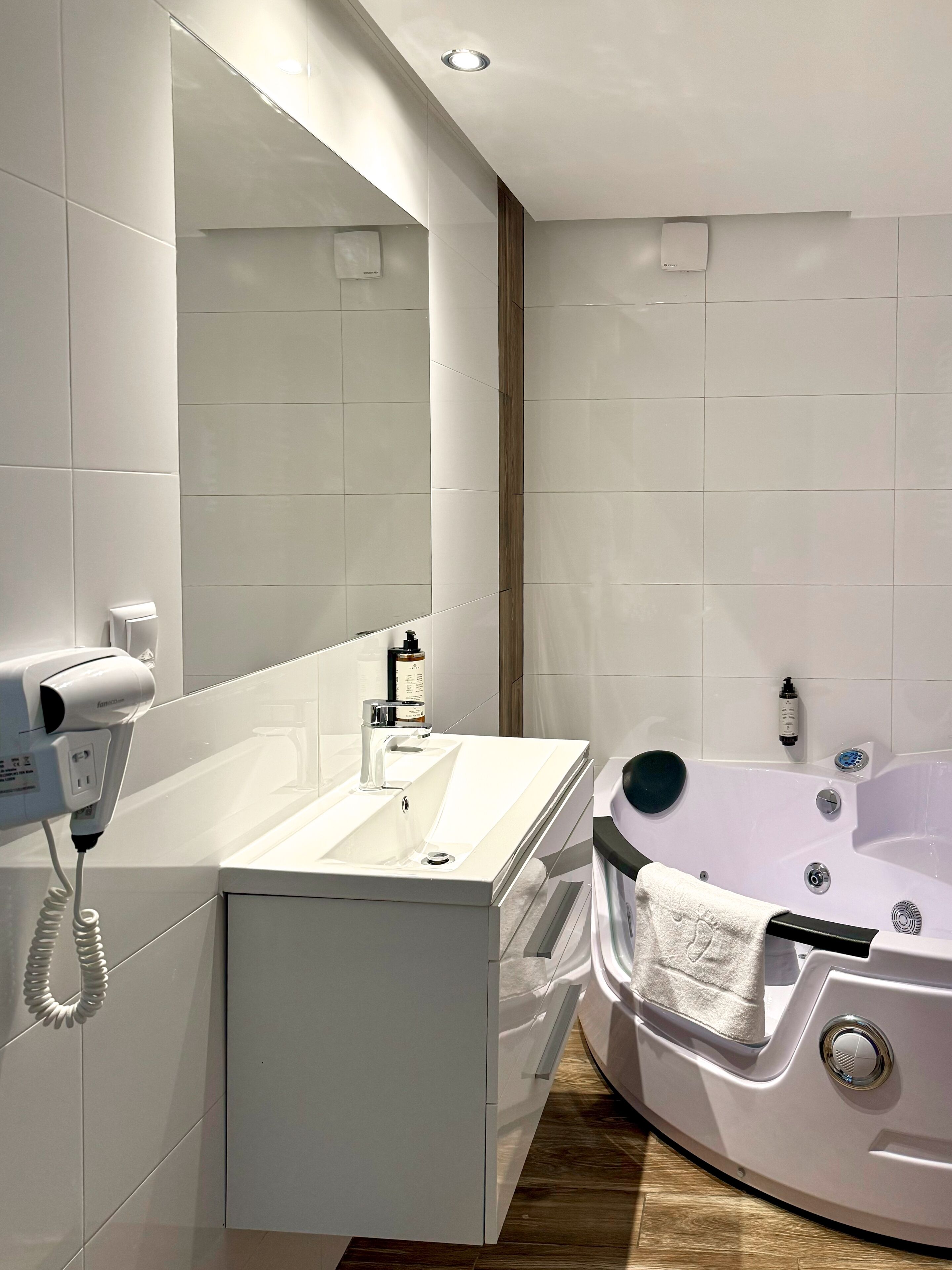 A modern bathroom with a white vanity, a large mirror, a hairdryer, a bathtub, and a towel rack.