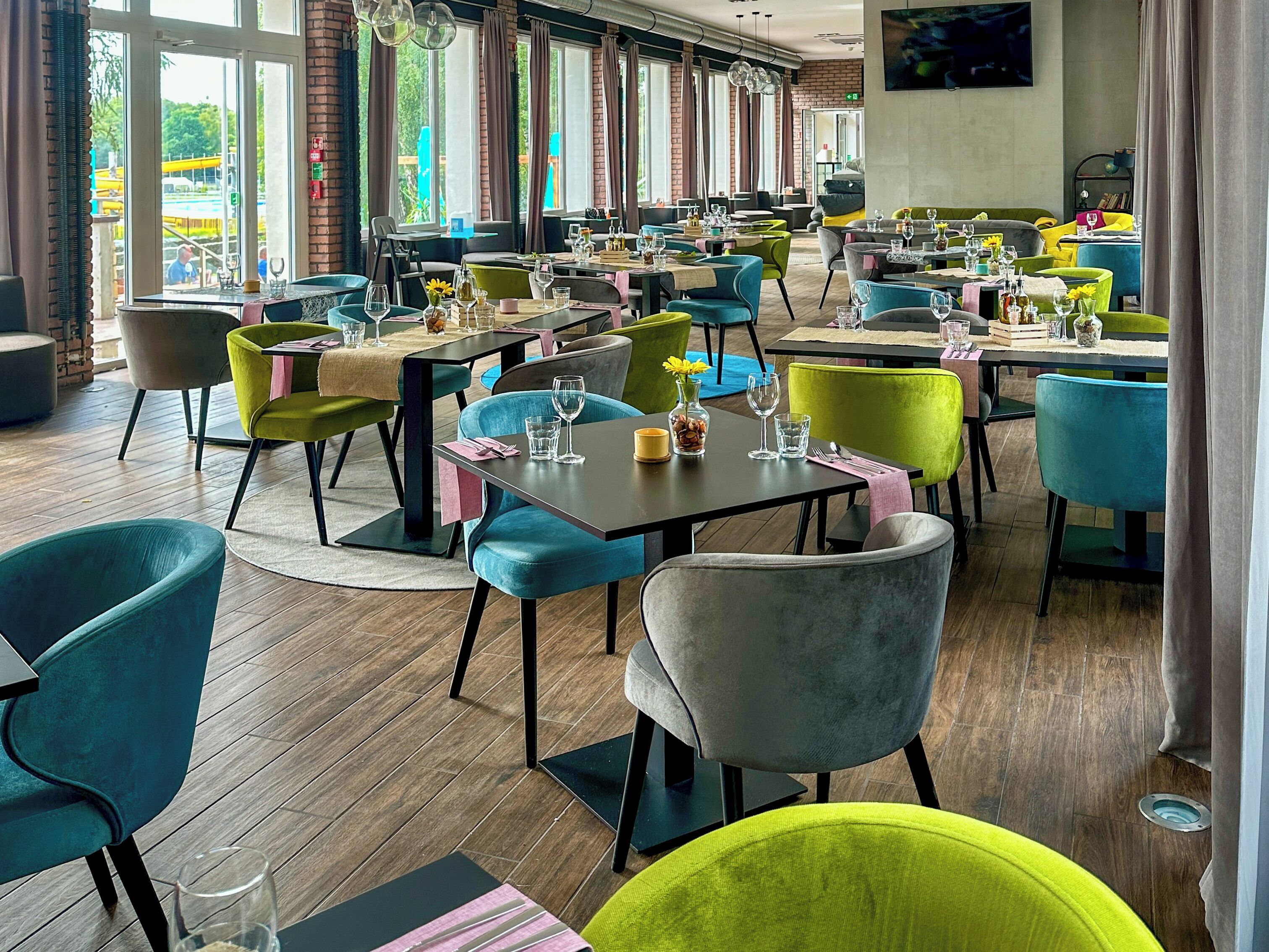 Un restaurante con varias mesas y sillas, ventanas amplias y una pared de ladrillo.