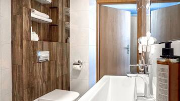 A modern bathroom with a wooden vanity, a toilet, and a large bathtub.