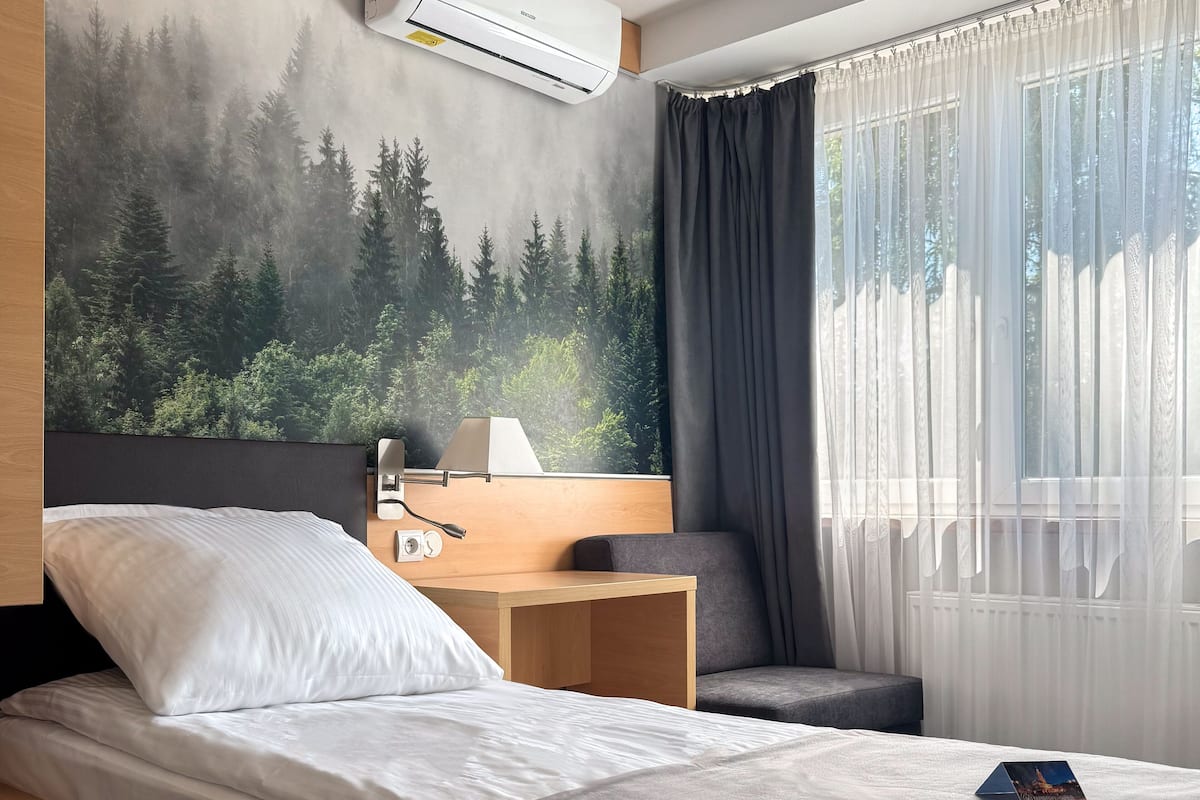 A hotel room with a bed, a desk, a chair, and a large forest mural on the wall.
