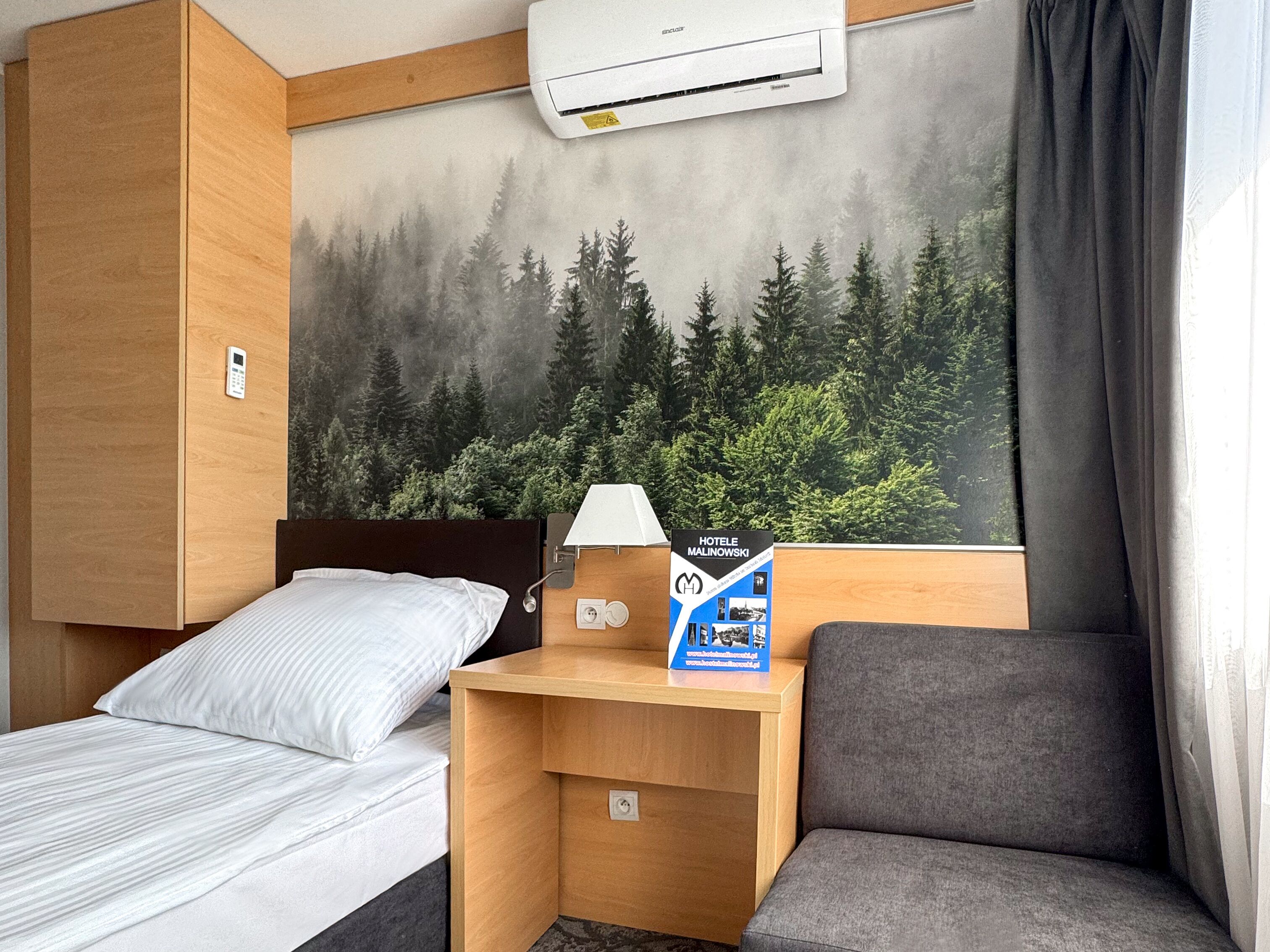Una habitación de hotel con cama, un escritorio con lámpara, aire acondicionado instalado en la pared y un cartel en la pared.