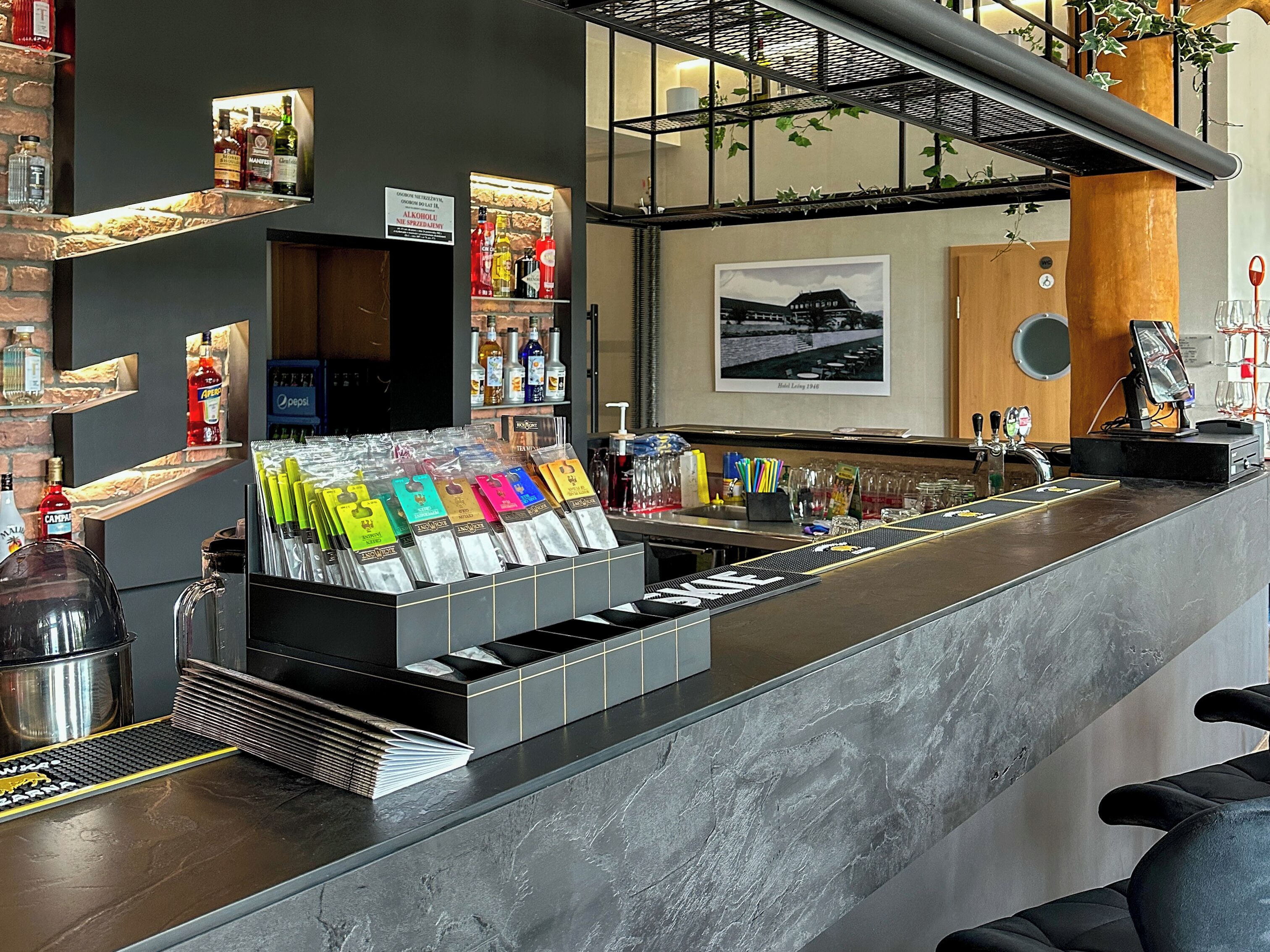 Una zona de bar con mostrador, estanterías llenas de botellas y una exhibición de objetos de colores.