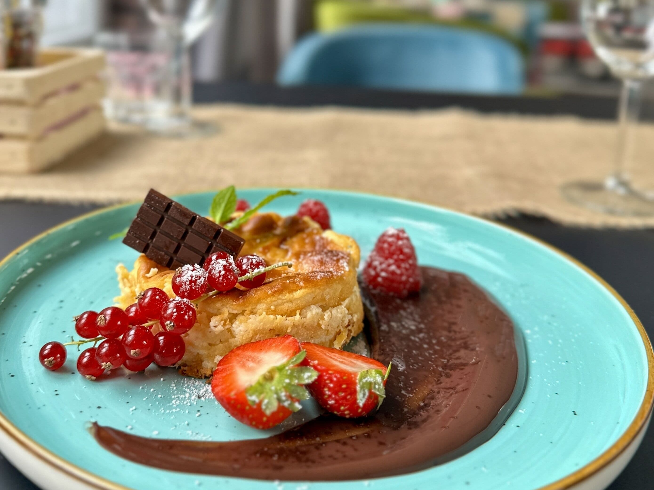 Un postre en un plato turquesa con grosellas rojas, fresas y chocolate.