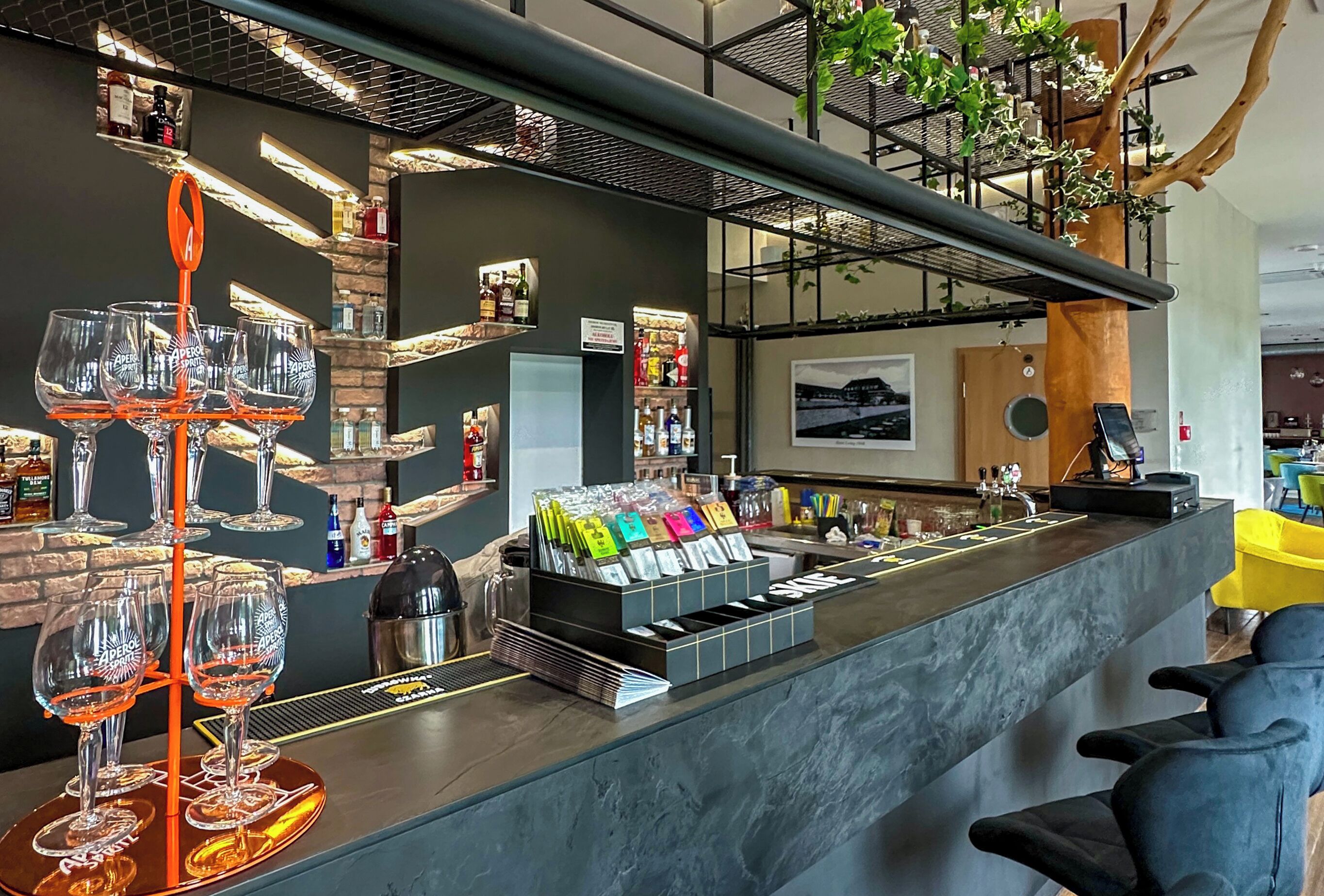 A bar area with a wine glass rack, a cash register, and a variety of bottles.