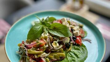 A plate of mixed salad with various vegetables and cheese, garnished with basil leaves, on a turquoise plate.
