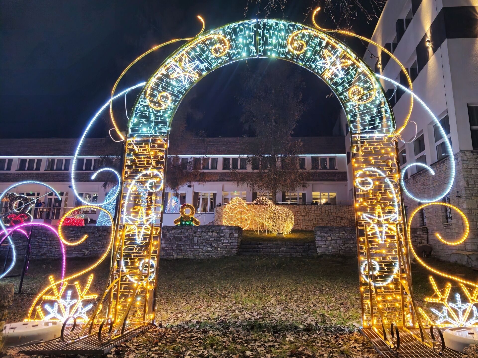An illuminated archway with decorative lights and a large teddy bear sculpture in the center.
