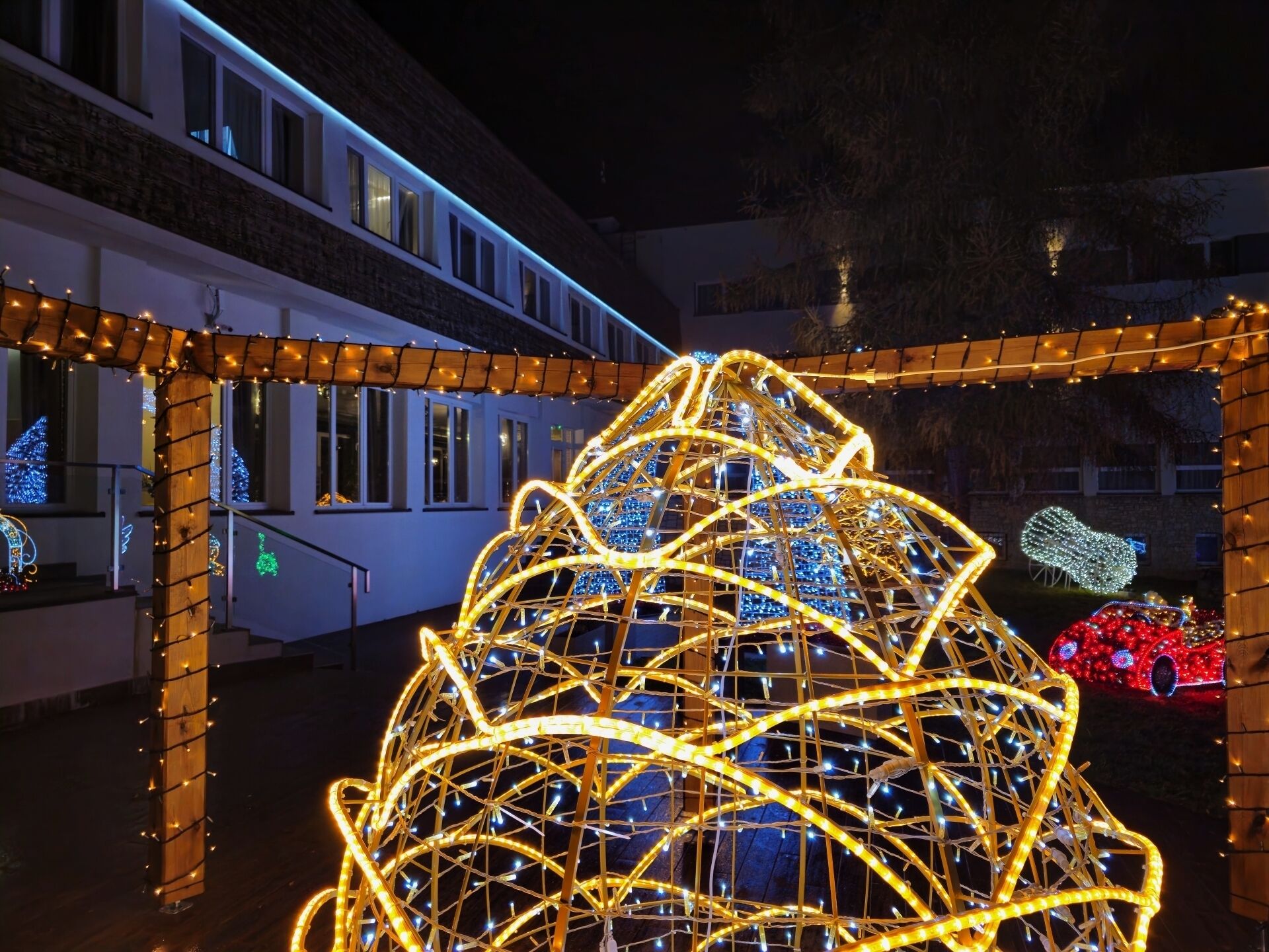 A building with a large illuminated structure resembling a geodesic dome, surrounded by string lights and a red car decoration.