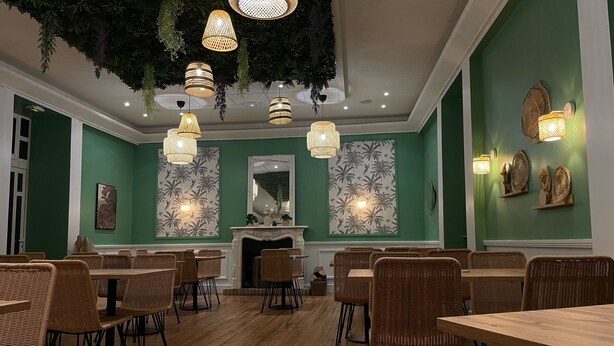 Un coin repas avec des meubles en osier, des murs verts et des luminaires suspendus.