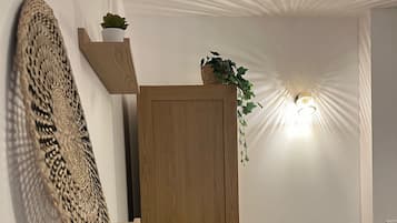 Une porte en bois surmontée d’une petite plante, un panier tressé posé sur une étagère et une table avec des chaises.