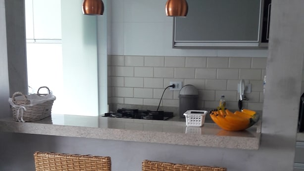 Uma cozinha moderna com duas cadeiras de vime, bancada e luminárias pendentes em cobre.
