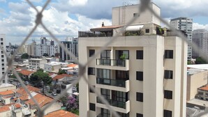 Um edifício de vários andares com varandas, uma combinação de edifícios residenciais e comerciais ao fundo, e um céu limpo.