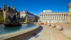 A public square with a fountain, a statue, and a large building with columns.