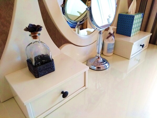 A vanity with a mirror, a tissue box, and a perfume bottle on a white dresser.