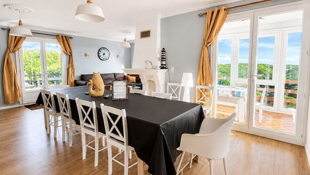 Un espace repas comprenant une table, des chaises et une vue sur la verdure grâce à de grandes fenêtres.