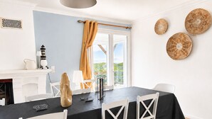 Un coin repas avec une nappe noire, des chaises blanches, une cheminée et une vue dégagée sur l’extérieur grâce à une grande fenêtre.