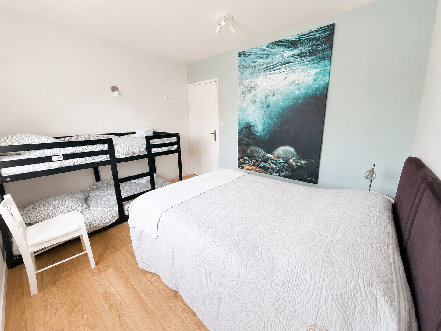 A room with bunk beds, a single bed, a chair, and a large abstract painting on the wall.