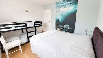 A room with bunk beds, a single bed, a chair, and a large abstract painting on the wall.