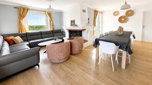 Un salon moderne comprenant un canapé, une table basse, un pouf, une table à manger, des chaises et une cheminée.