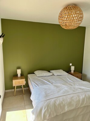 Une chambre à coucher avec un lit, deux tables de chevet, un luminaire suspendu et un mur vert.