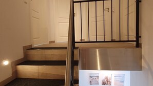 Eine Treppe mit Metallhandläufer, eine Zwischenebene mit einer Stützsäule aus Edelstahl und eine Tür im Hintergrund.