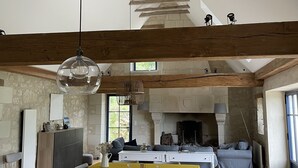 A spacious living area with a high ceiling, exposed wooden beams, a central fireplace, and a dining area with a yellow tablecloth. - Wunderschönes Landhaus Atemberaubende Aussicht (Huismes)