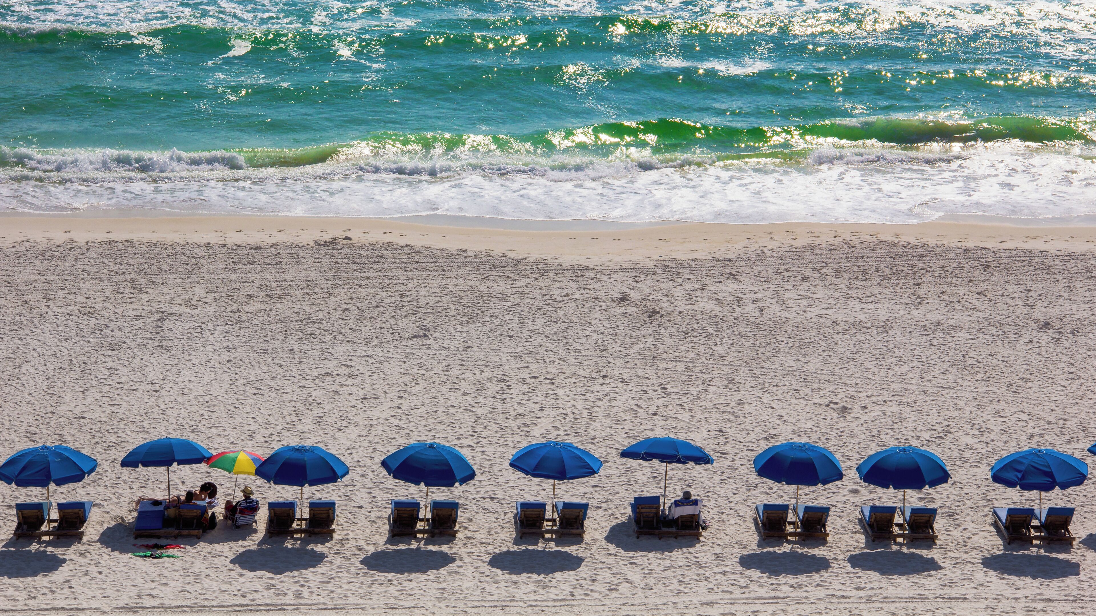 A beach with rows of blue umbrellas and wooden lounge chairs.