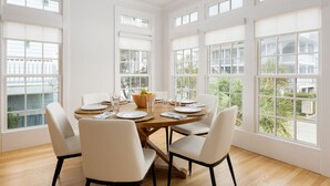 Une salle à manger avec une table ronde dressée pour six personnes, de grandes fenêtres et une vue sur l’extérieur.