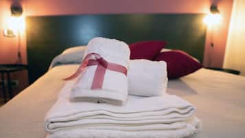 A neatly made bed with white towels and a pink ribbon, a red pillow, and two wall-mounted lights.