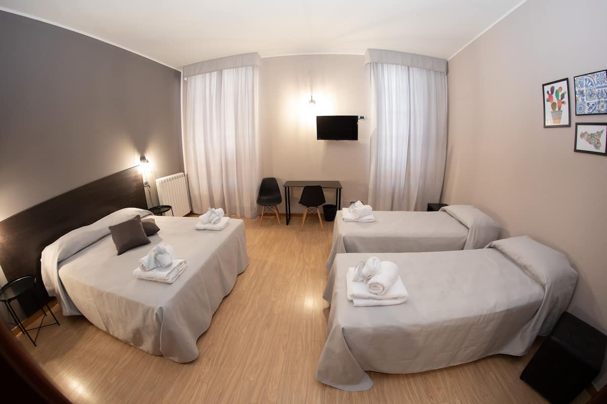 A hotel room with two single beds, a desk, a chair, a TV, and artwork on the wall.
