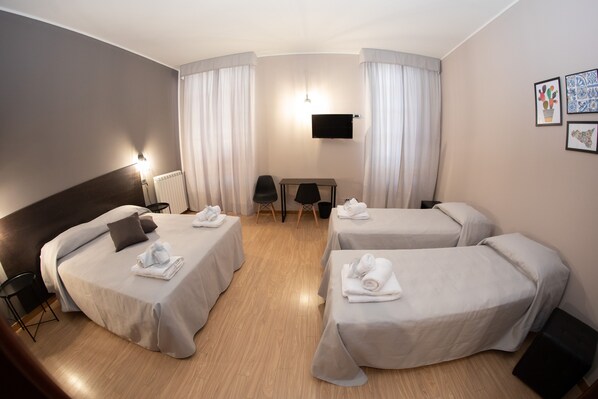 Une chambre d’hôtel avec deux lits simples, un bureau, une chaise, une télévision et des œuvres d’art accrochées au mur.