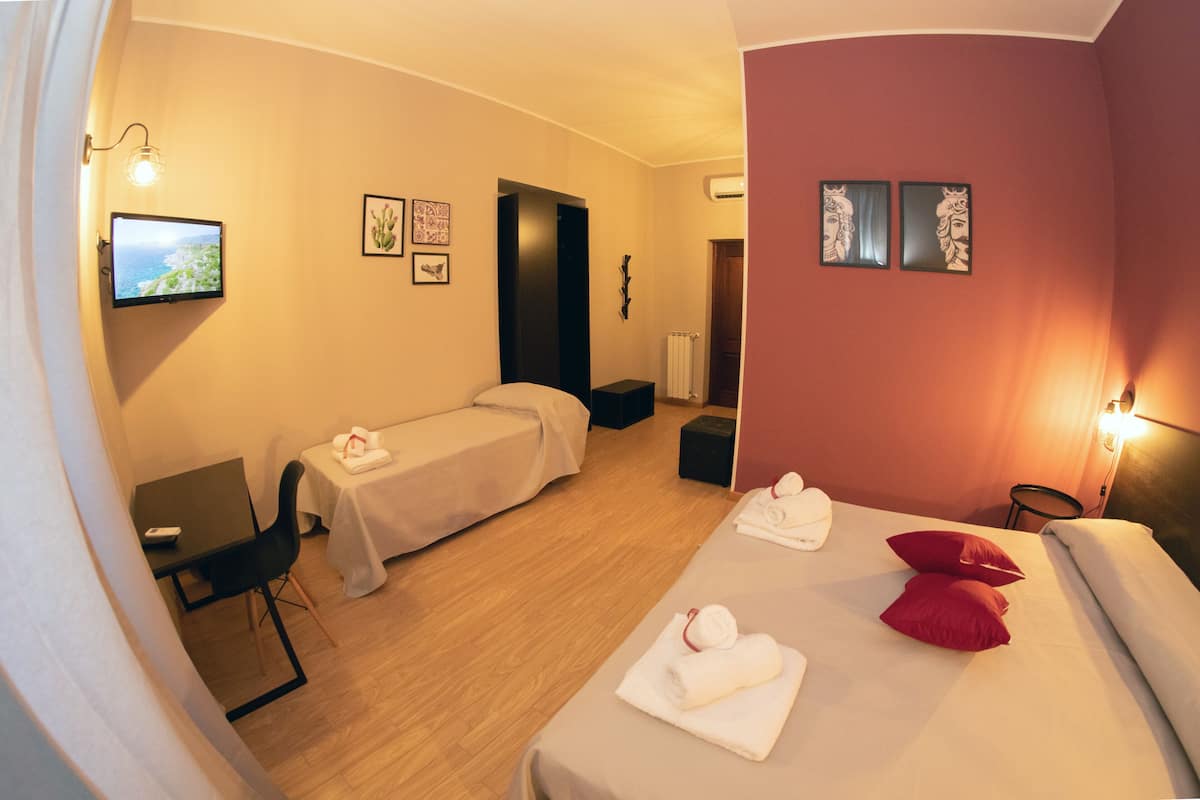 A hotel room with a bed, a desk, a chair, a small table, and a TV.