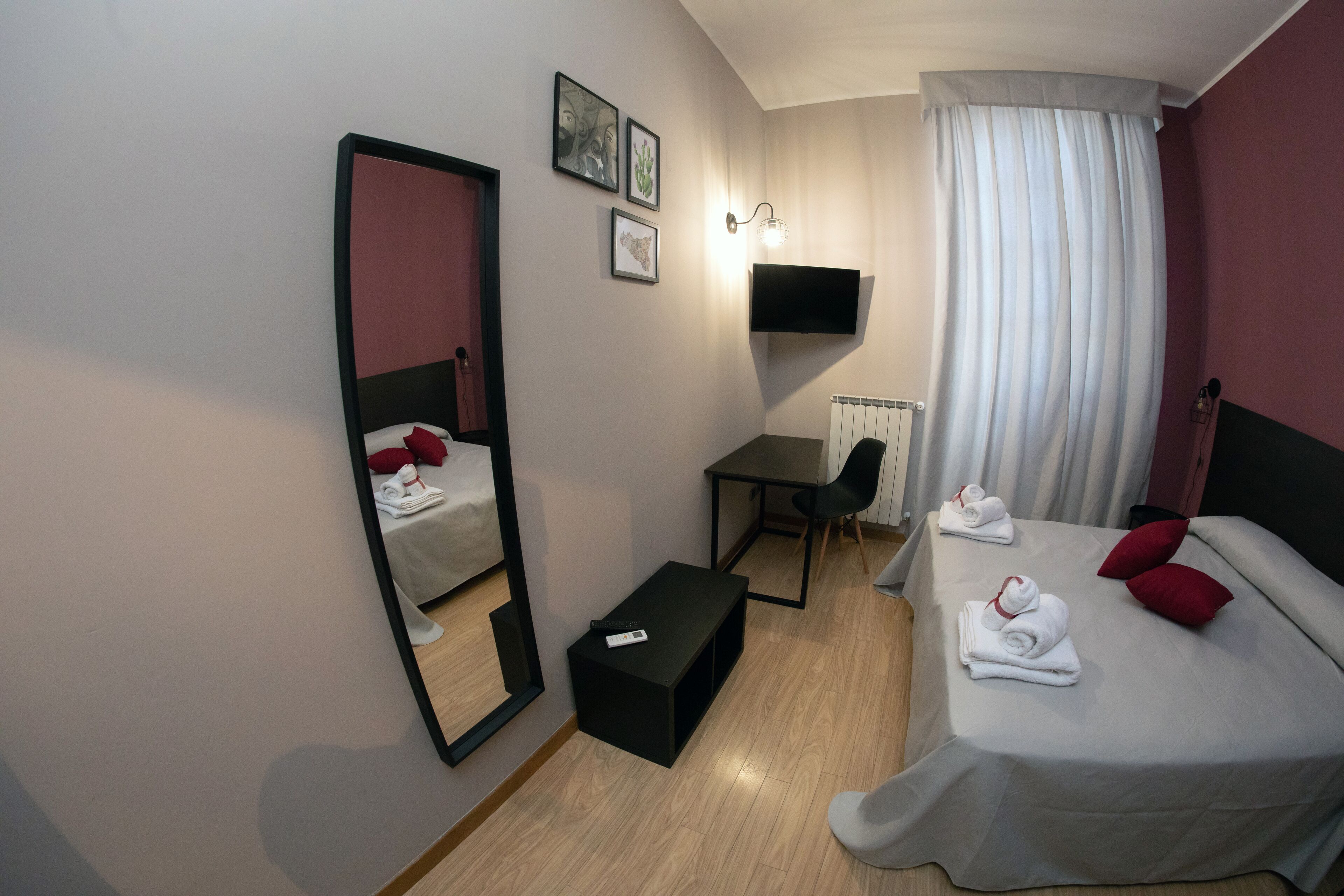 A hotel room with a bed, a desk, a chair, a TV, and a mirror.